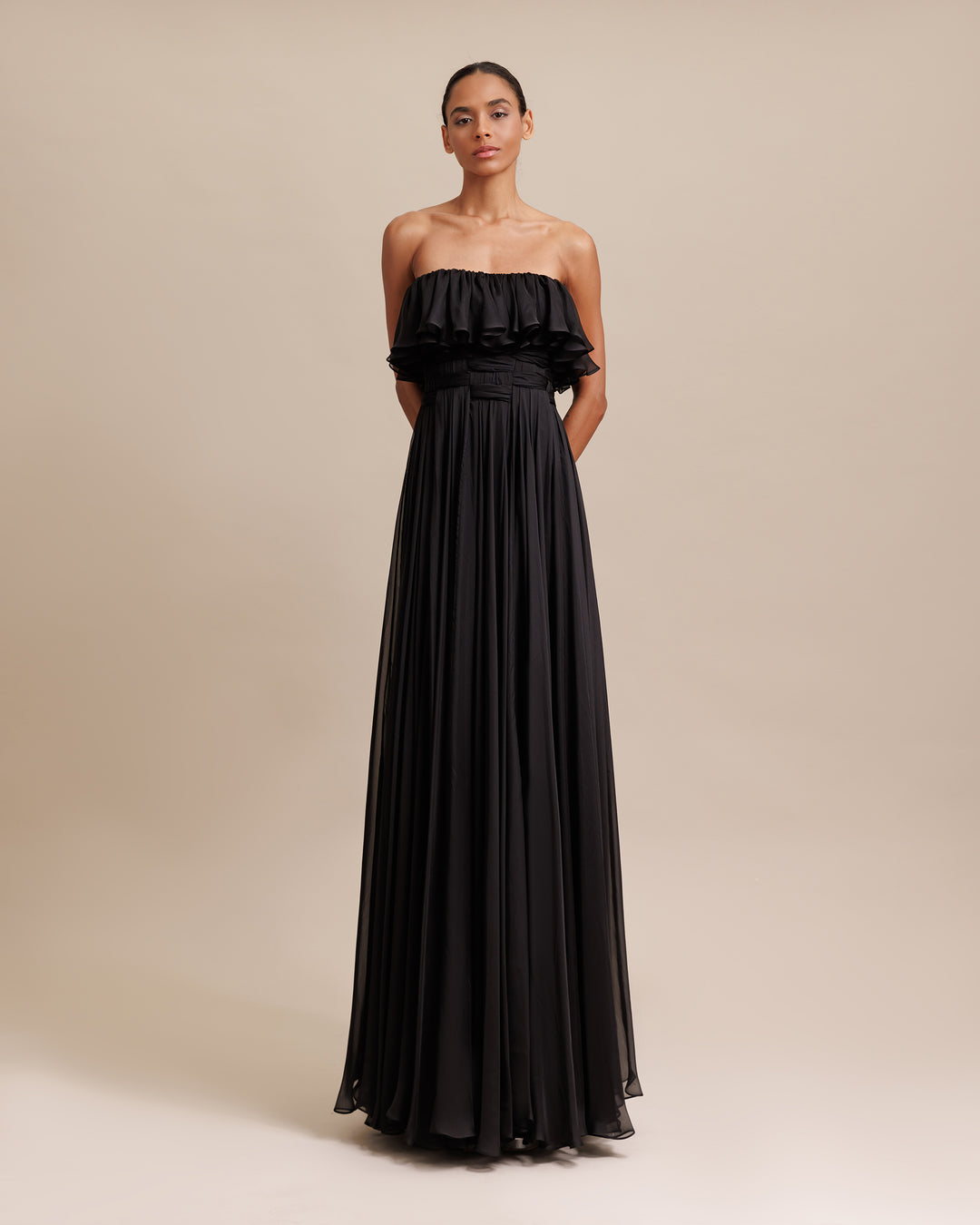 A strapless cut flared chiffon long black evening dress with ruffle bust and draping details.