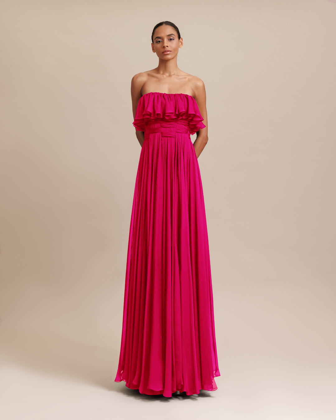 A strapless cut flared chiffon long fuchsia dress with ruffles on the bust and draping details.