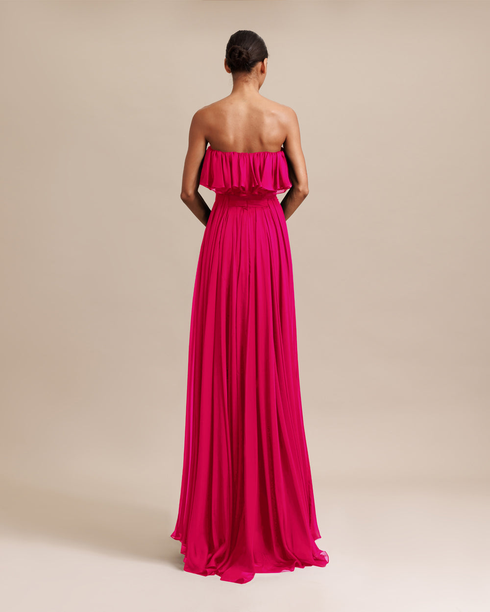 The back of a strapless cut flared chiffon long fuchsia dress with ruffles on the bust and draping details.