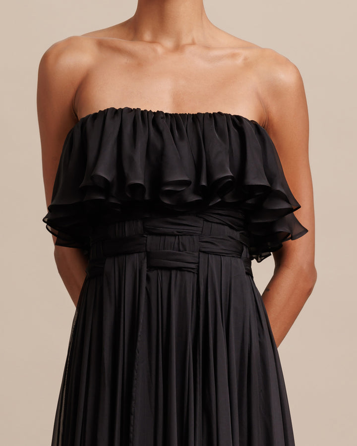 A close-up of a strapless cut flared chiffon long black evening dress with ruffles bust and draping details.