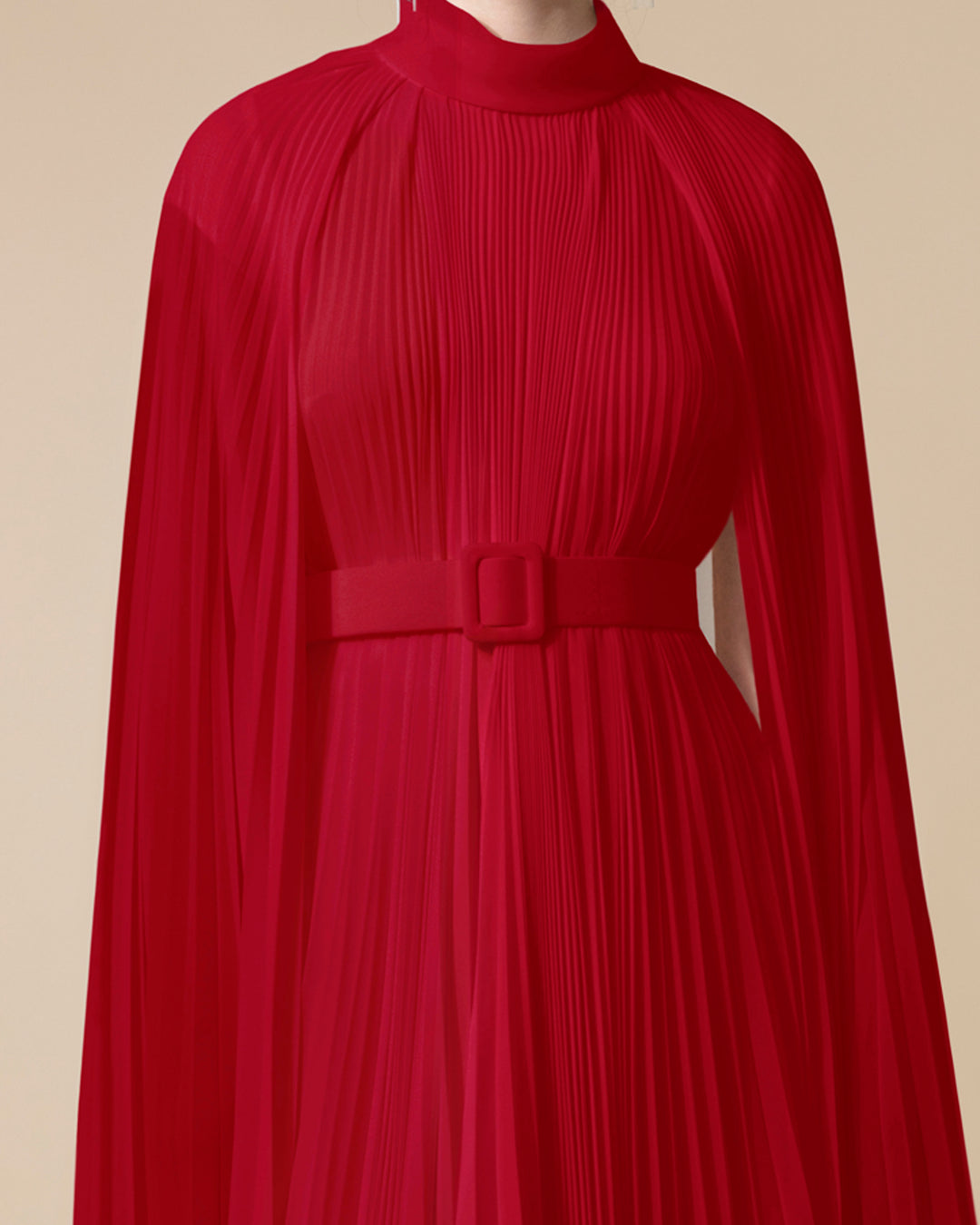 A close-up of a fully pleated chiffon kaftan dress in red color with cape-like asymmetrical sleeves and a matching detachable belt.