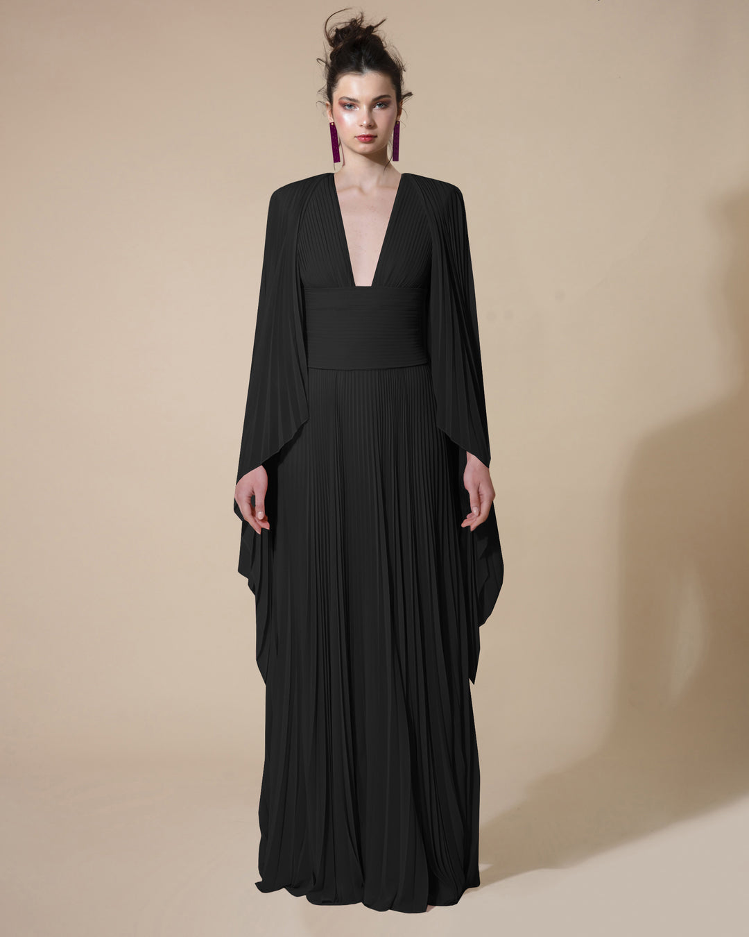 A fully pleated black evening dress with a deep V-neck fitted on the waist with a draped over layer and a side slit.