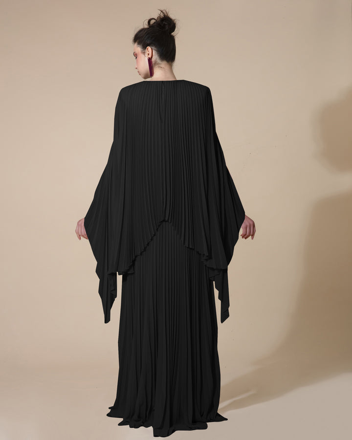 The back of a fully pleated black evening dress with uneven cape-like sleeve.