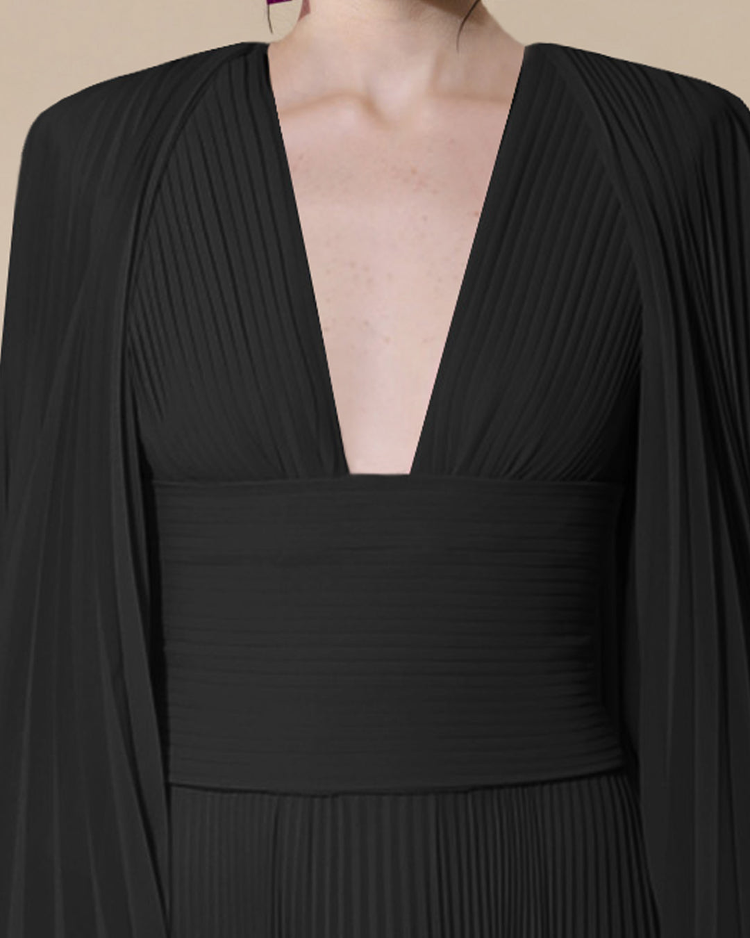 A close-up of a fully pleated black evening dress with a deep V-neck fitted on the waist with a draped over layer.