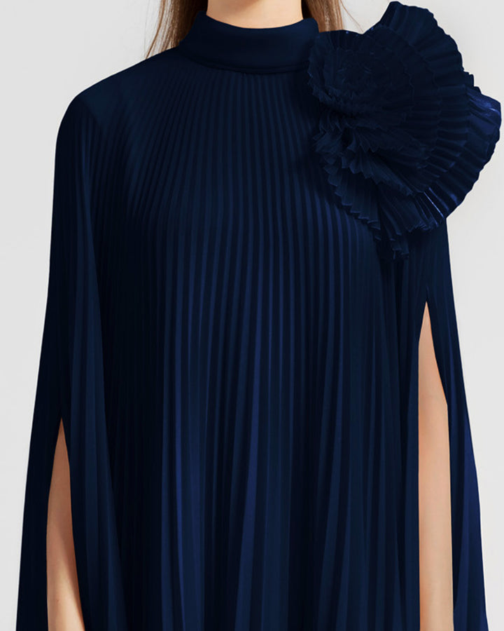 A close-up of a fully pleated lame organza flared navy kaftan dress with an embellished draped flower on the shoulder.