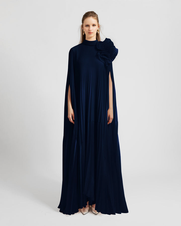 A fully pleated lame organza flared navy kaftan dress with an embellished draped flower on the shoulder.