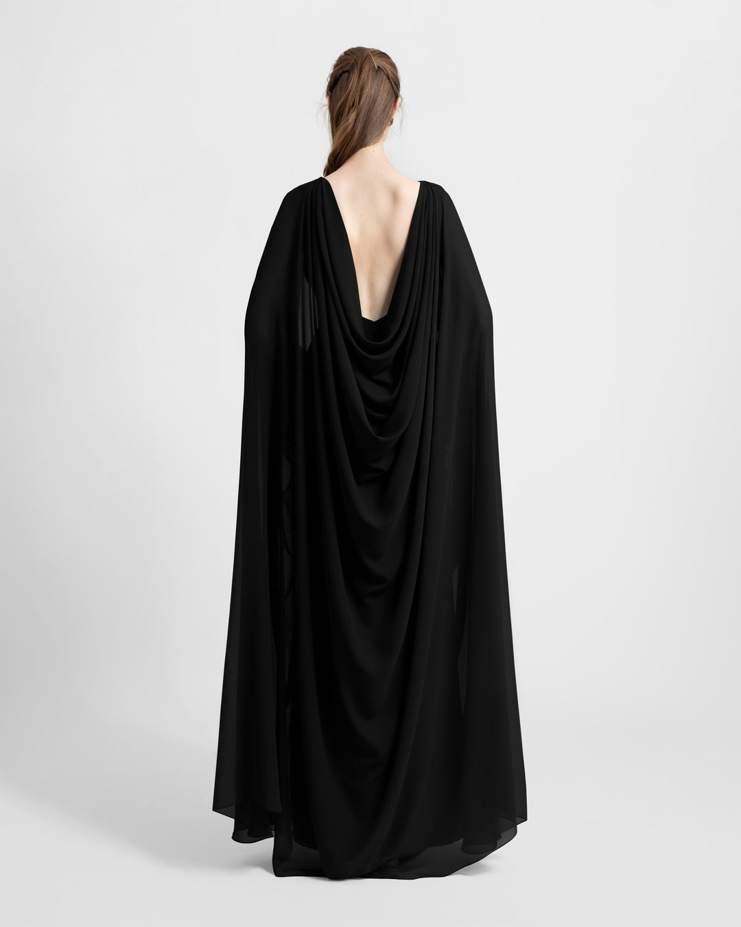 The back of an open-back black evening dress with a chiffon cape-like sleeves.