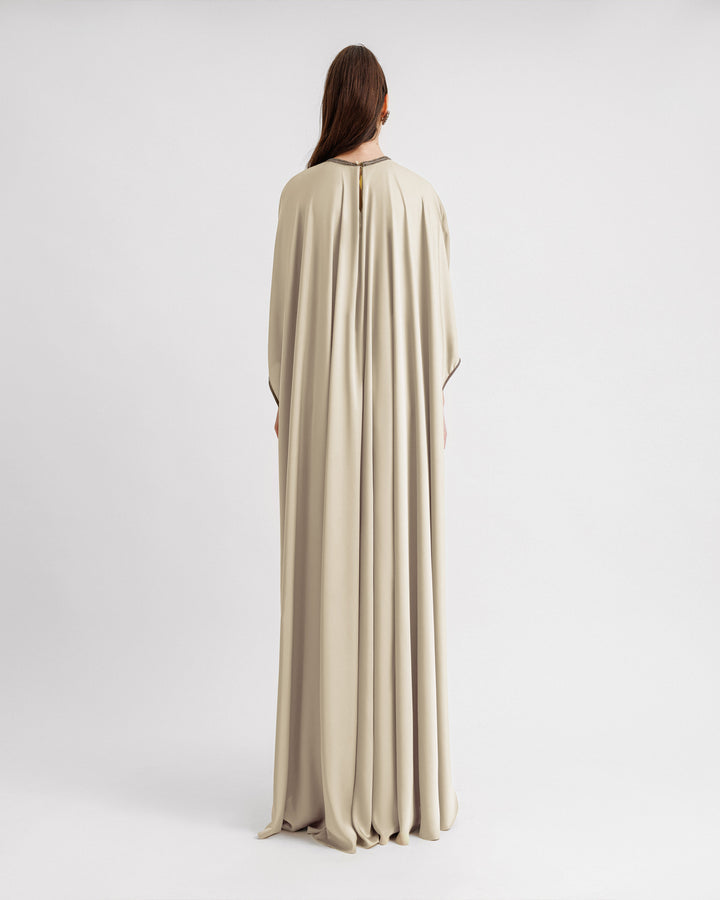 The back of a cream satin kaftan-style evening dress with a draped beaded neckline, featuring three-quarters sleeves with beaded cuffs.