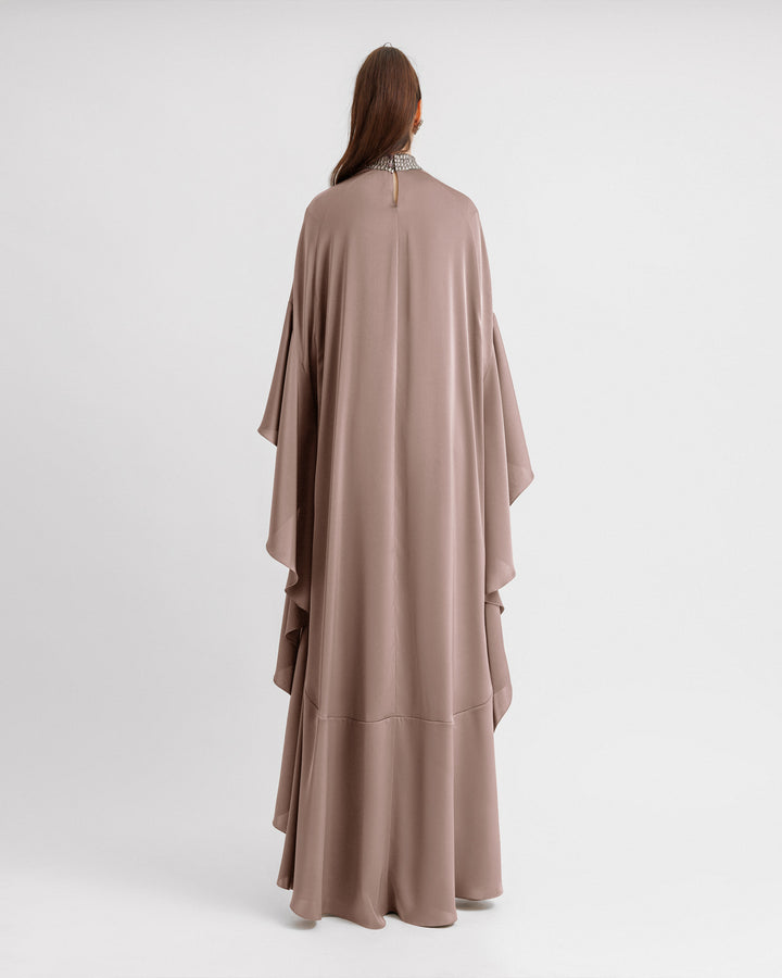 The back of a kaftan-style evening dress in taupe color with a beaded collar and ruffled floor-length sleeves.