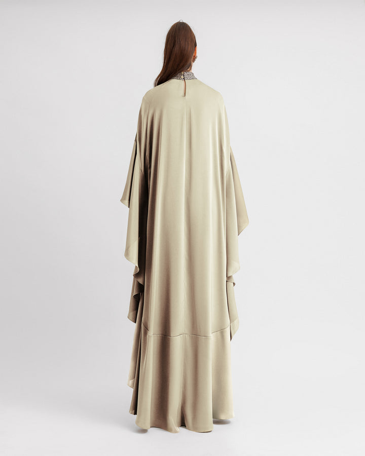 The back of a kaftan-style evening dress in cream color satin with a beaded collar and ruffled floor-length sleeves.