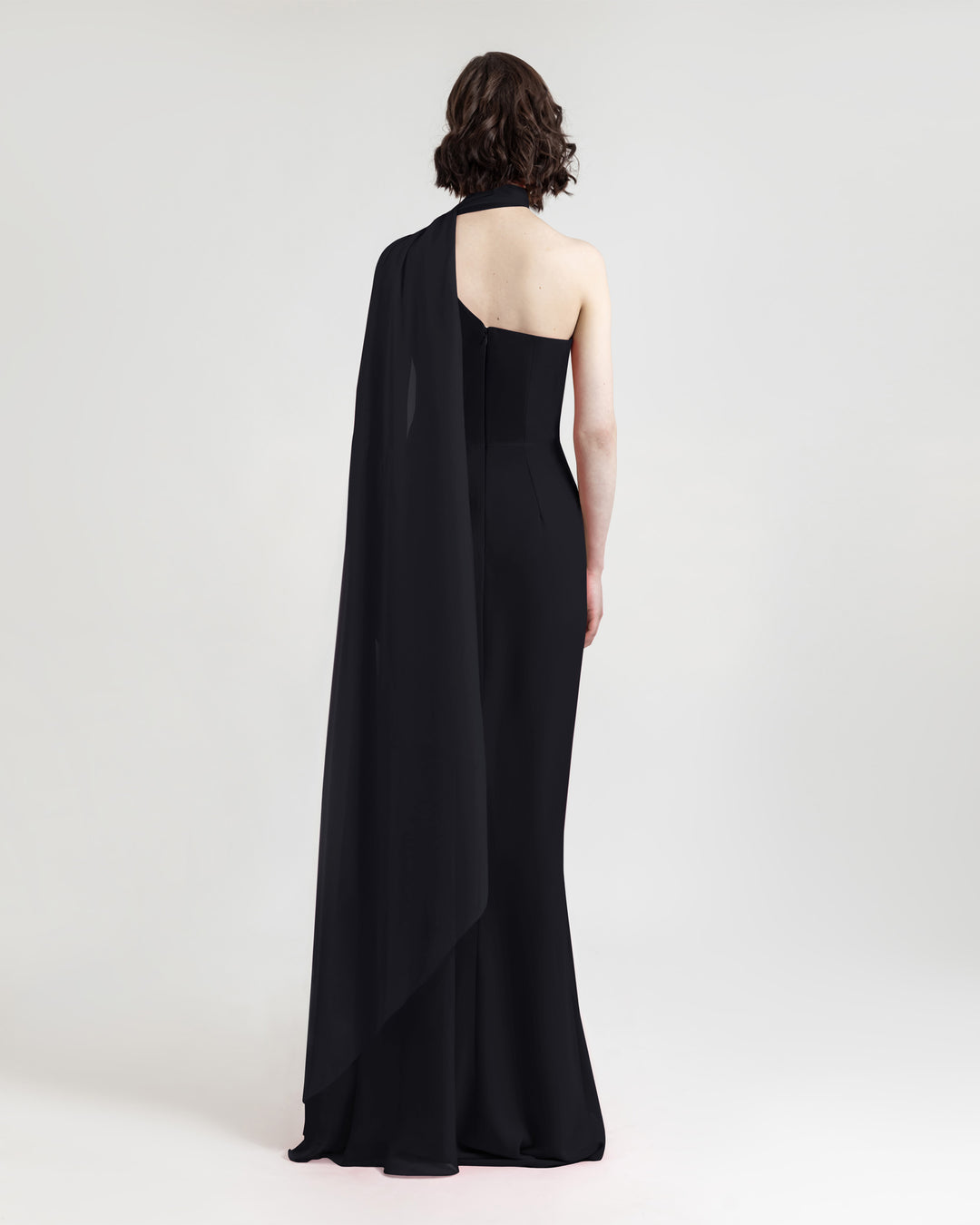 The back of an asymmetrical shawl collar black evening dress featuring an open back.