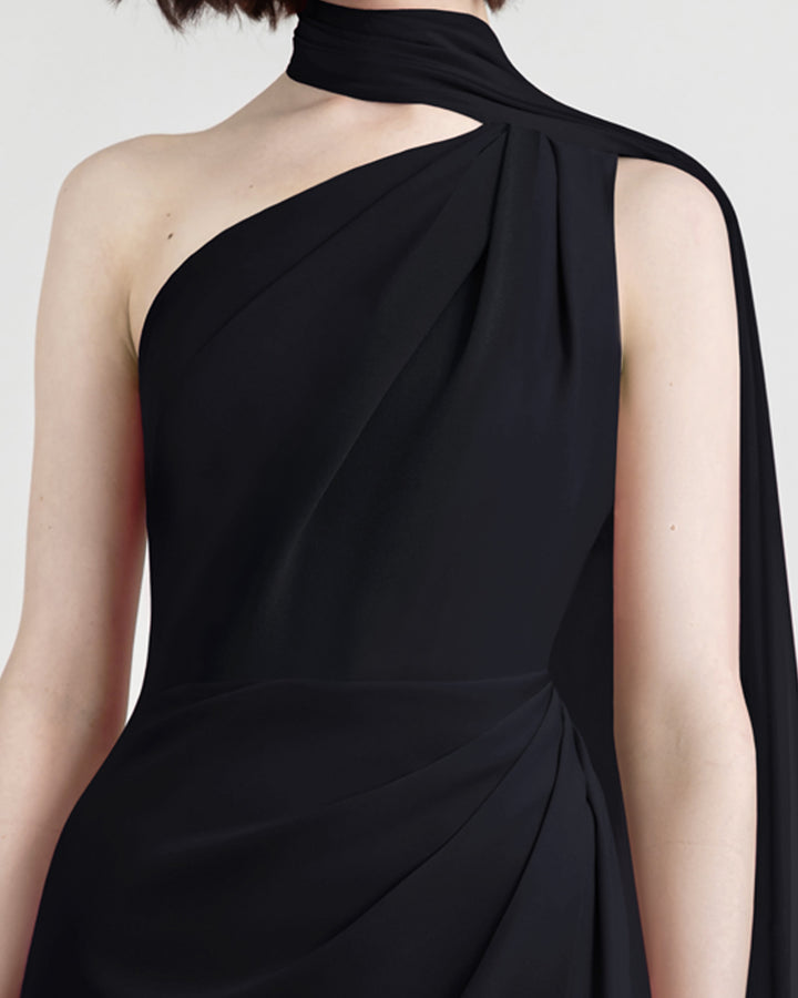 A close-up of an asymmetrical shawl collar black evening dress with draping details on the shoulder and the waist.