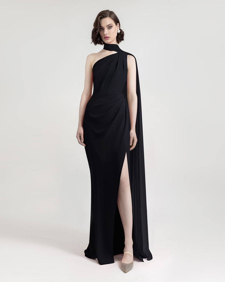 An asymmetrical floor length shawl collar black evening dress with draping details on the shoulder and the waist. It features an open slit on the side.