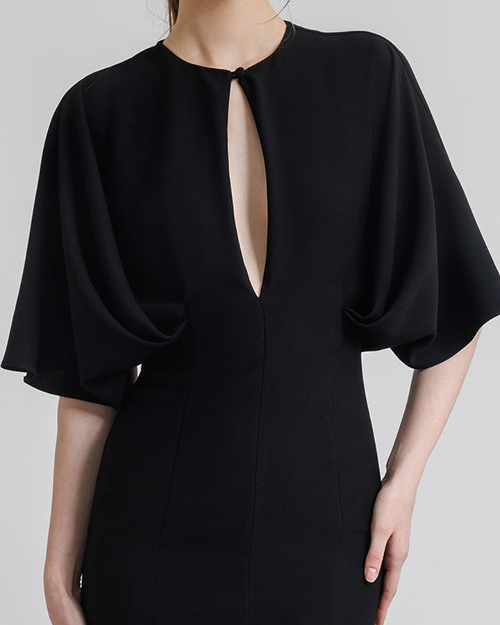 A close-up of a slim-cut black evening dress with a front opening on the bust area, wide cape-like sleeves, and an open lower back.