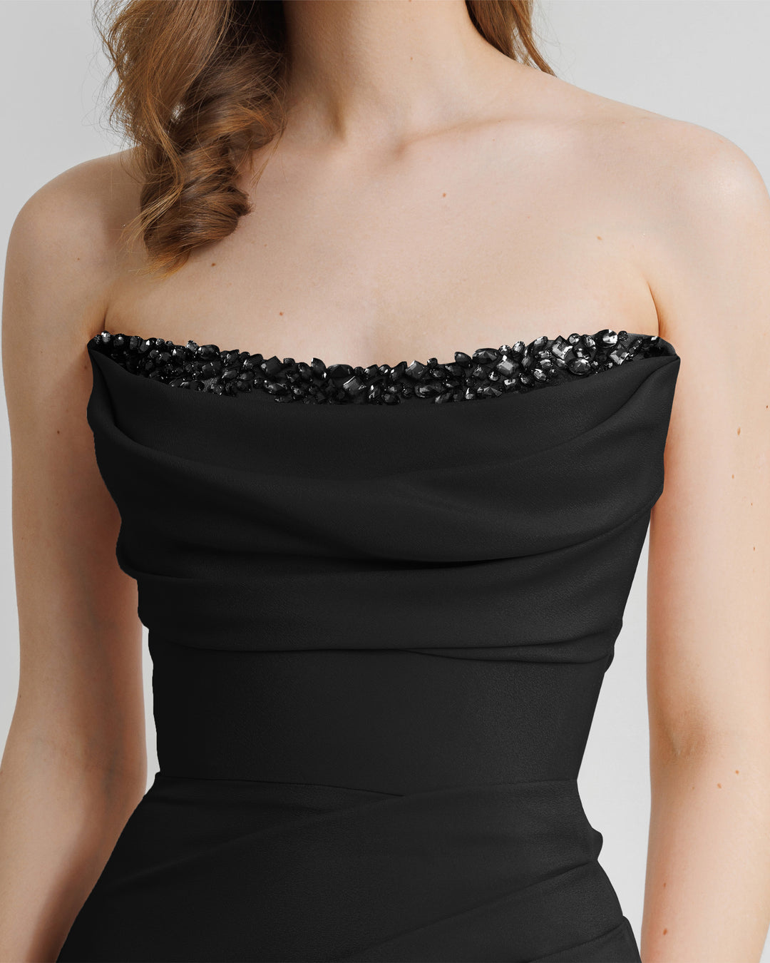 A close-up of a strapless, straight cut long black evening dress, with beading details on the bust line, and draping details.