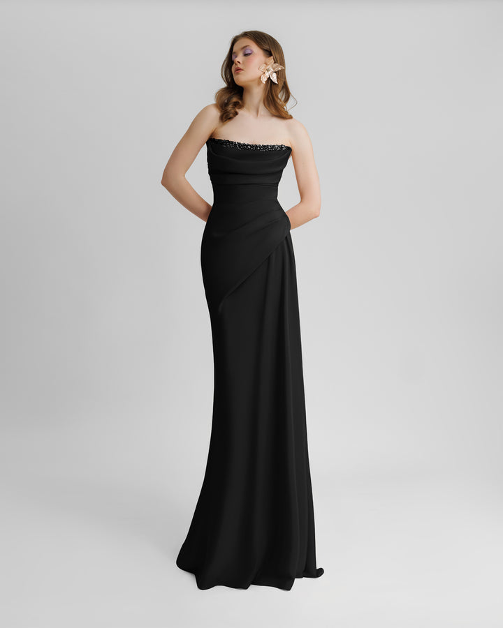 A strapless, straight cut long black evening dress, with beading details on the bust line, and some draping details from the bust going down the waist.