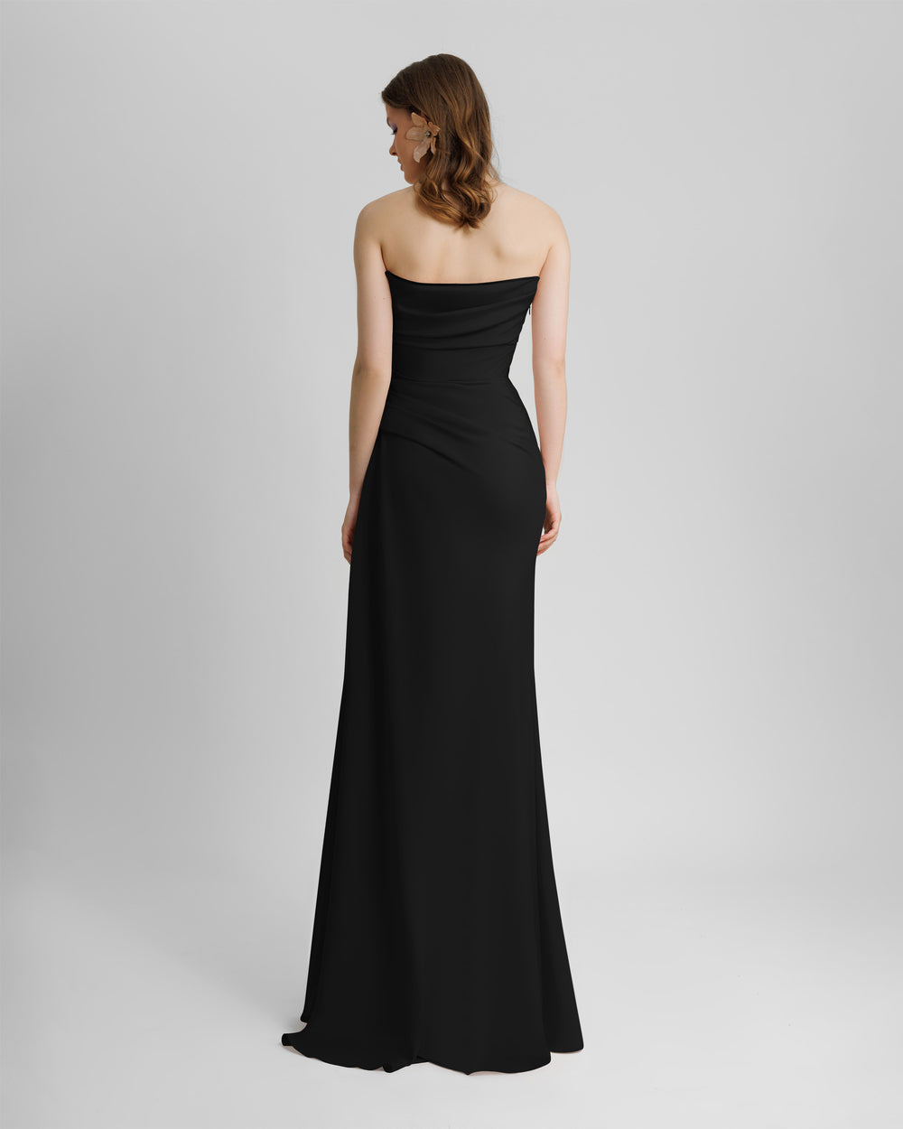 The back of a strapless, straight cut long black evening dress, with draping details from the bust going down the waist.