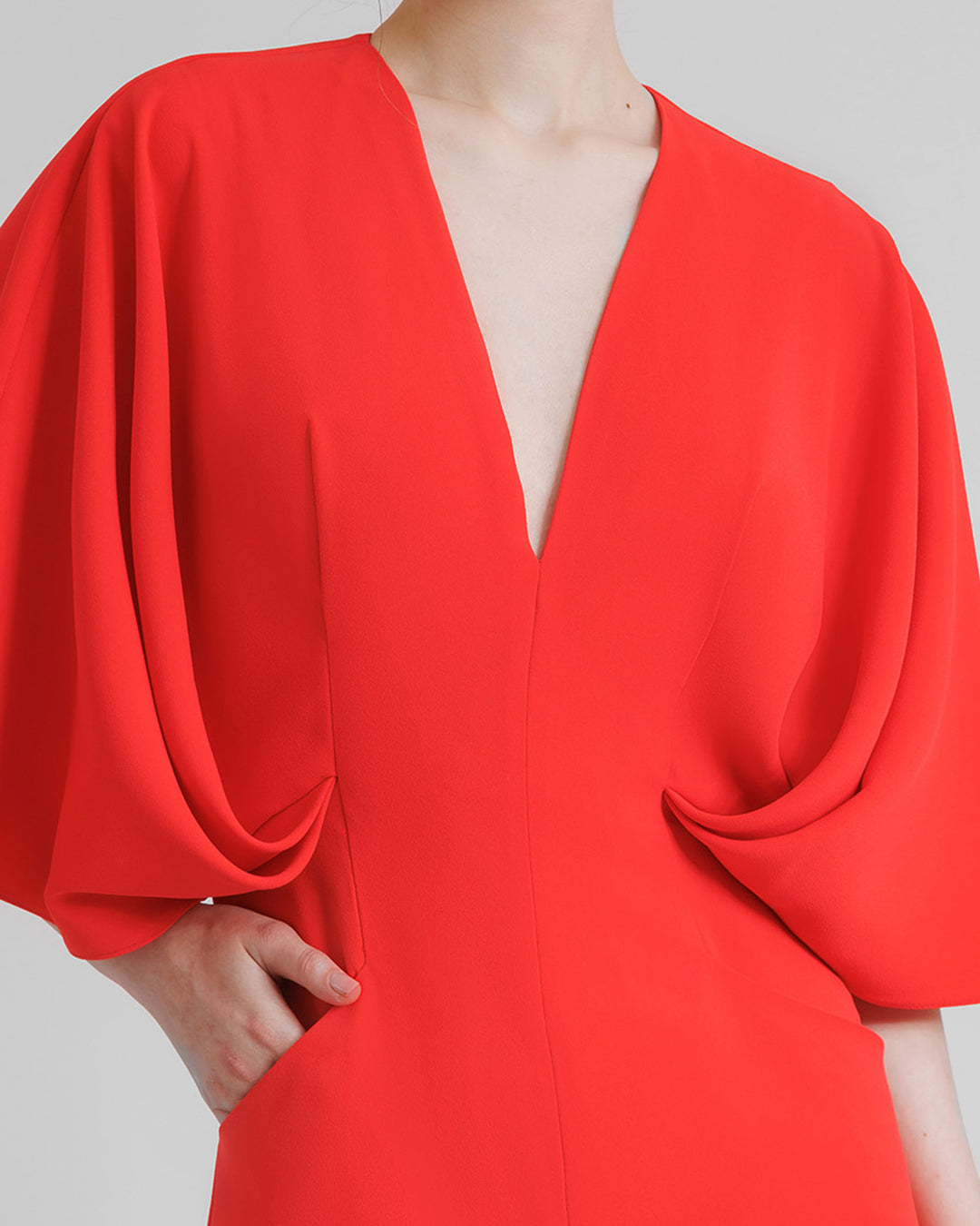 A close-up of a v-neckline flared coral jumpsuit with wide draped cape like sleeves.