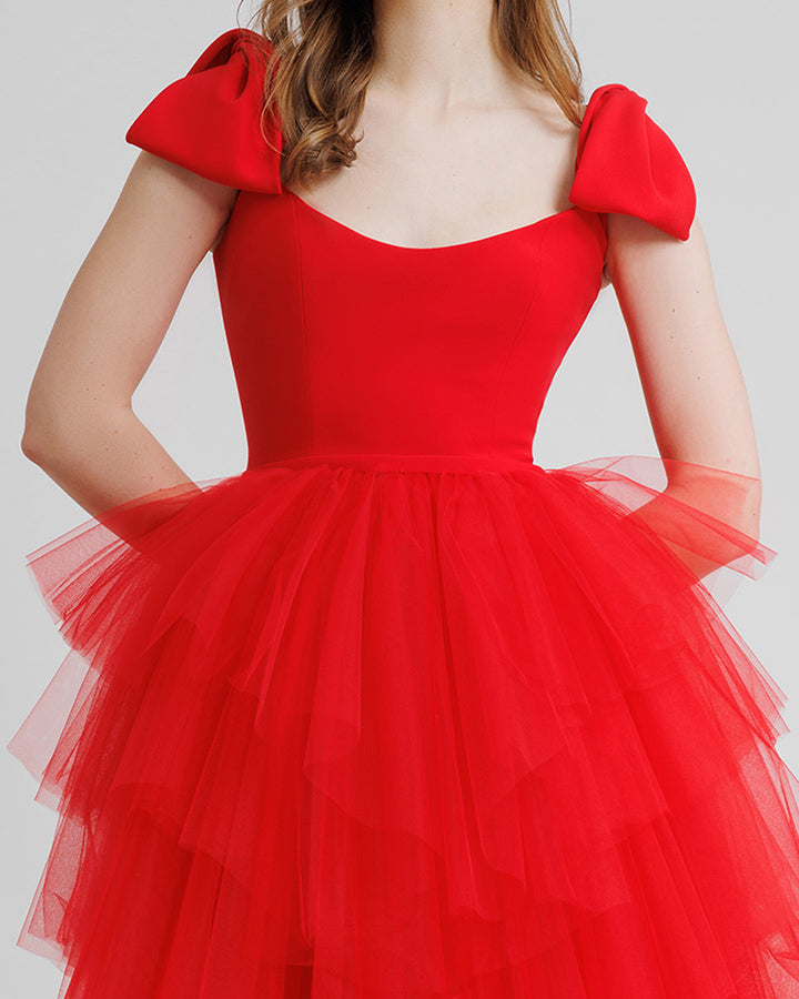 A close-up of a long red evening dress with bow designs on the shoulders and asymmetrical rushed tulle layered skirt.