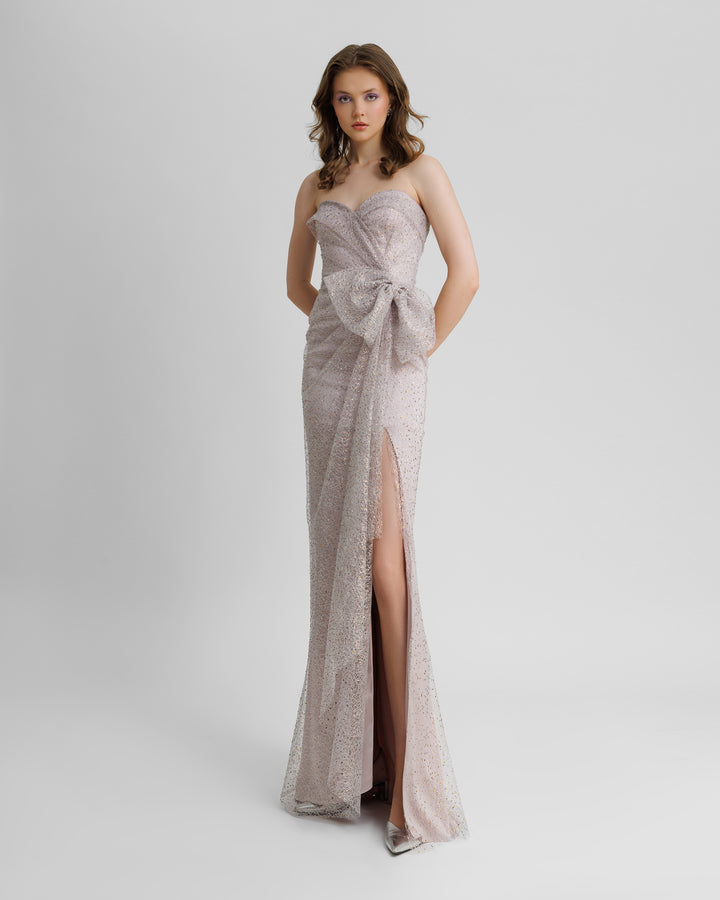 A strapless dubetti-like bodice long lilac evening dress with draping details, a bow design on the waist, and a slit on the side.