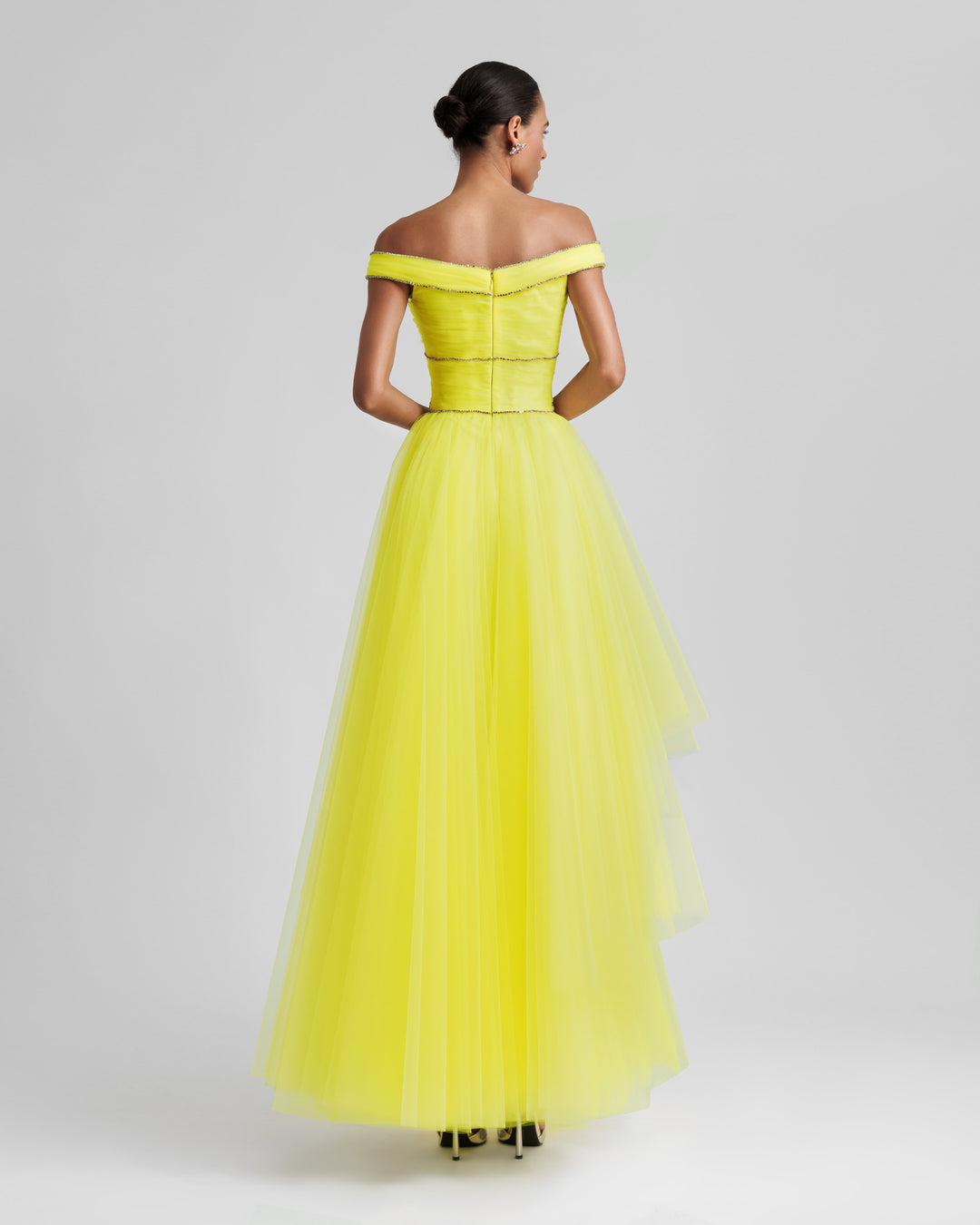 The back of an off-the-shoulders evening yellow dress with beaded trimmings on the corset and an asymmetrical layered tulle skirt.