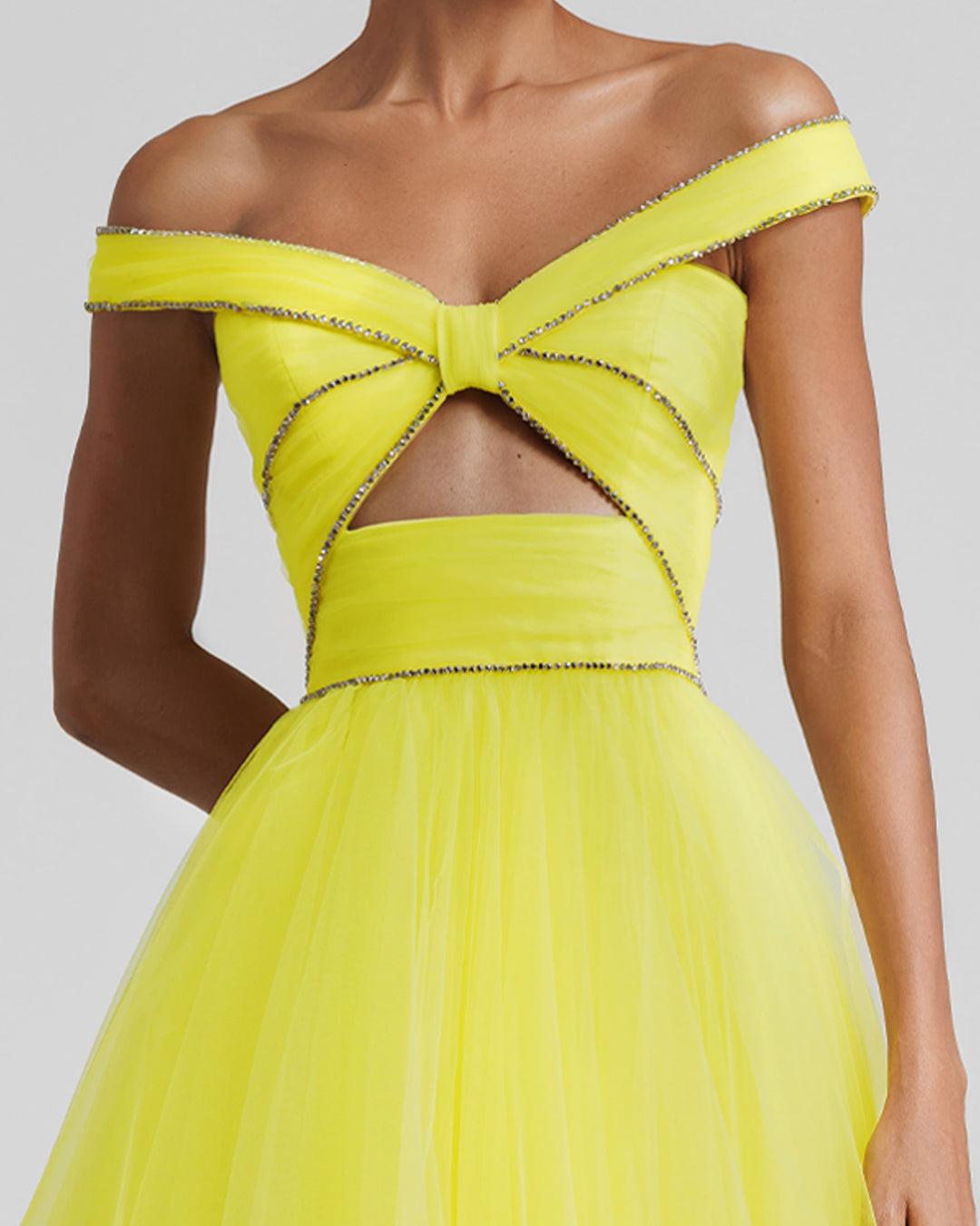 A close-up of an off-the-shoulders evening yellow dress with beaded trimmings on the corset, a cut-out at the front, and an asymmetrical layered tulle skirt.