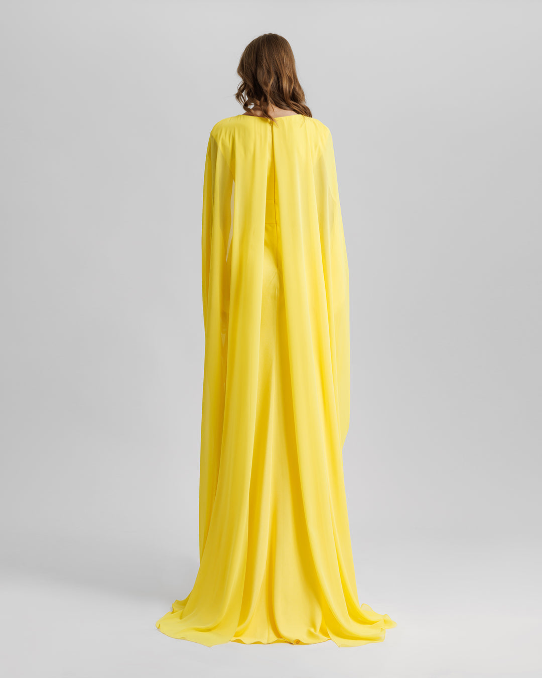 The back of a long yellow evening dress with cape-like draped sleeves.