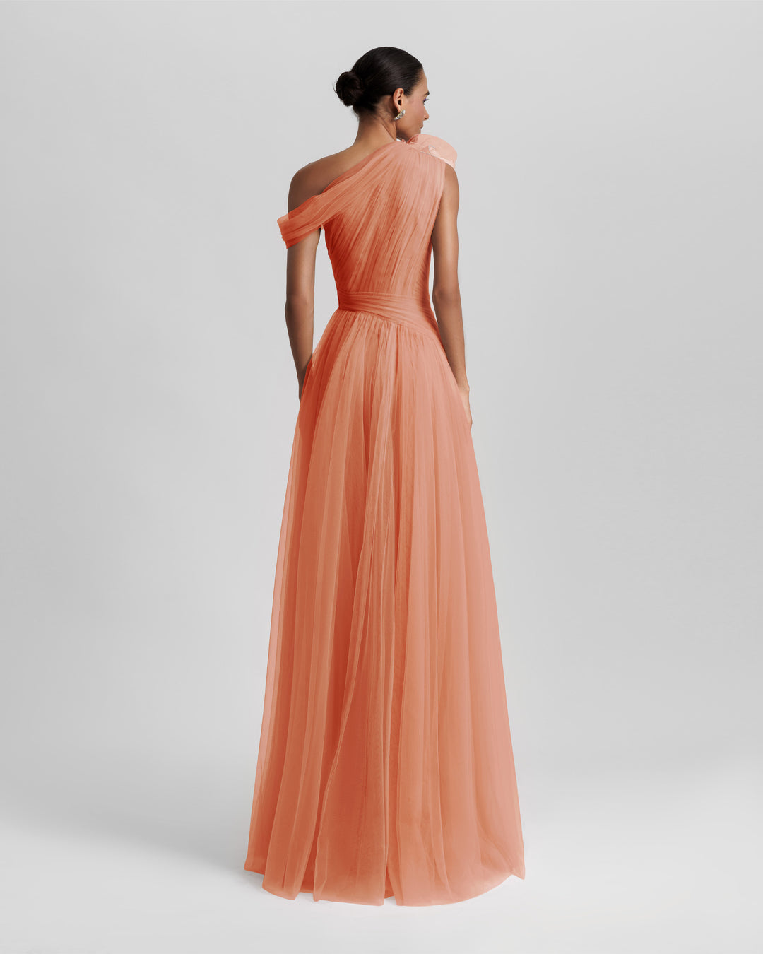 The back of an asymmetrical neckline full tulle long evening dress in peach color, with draping design on the bodice.