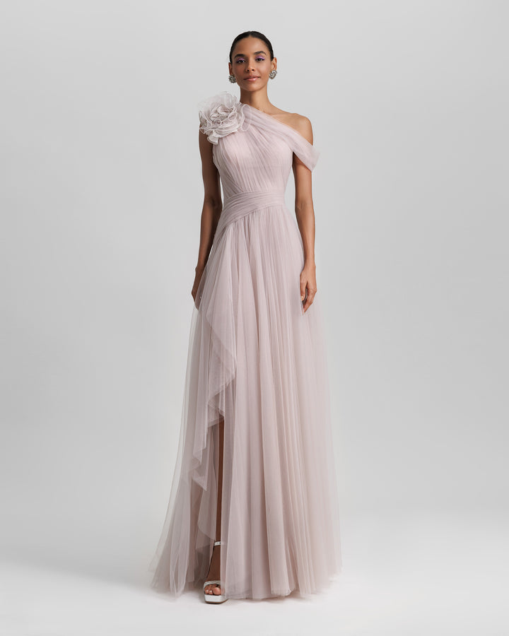 A full tulle long evening dress, with an asymmetrical neckline, a flower design on the shoulder, a ruffled side slit, and draping design on the bodice.