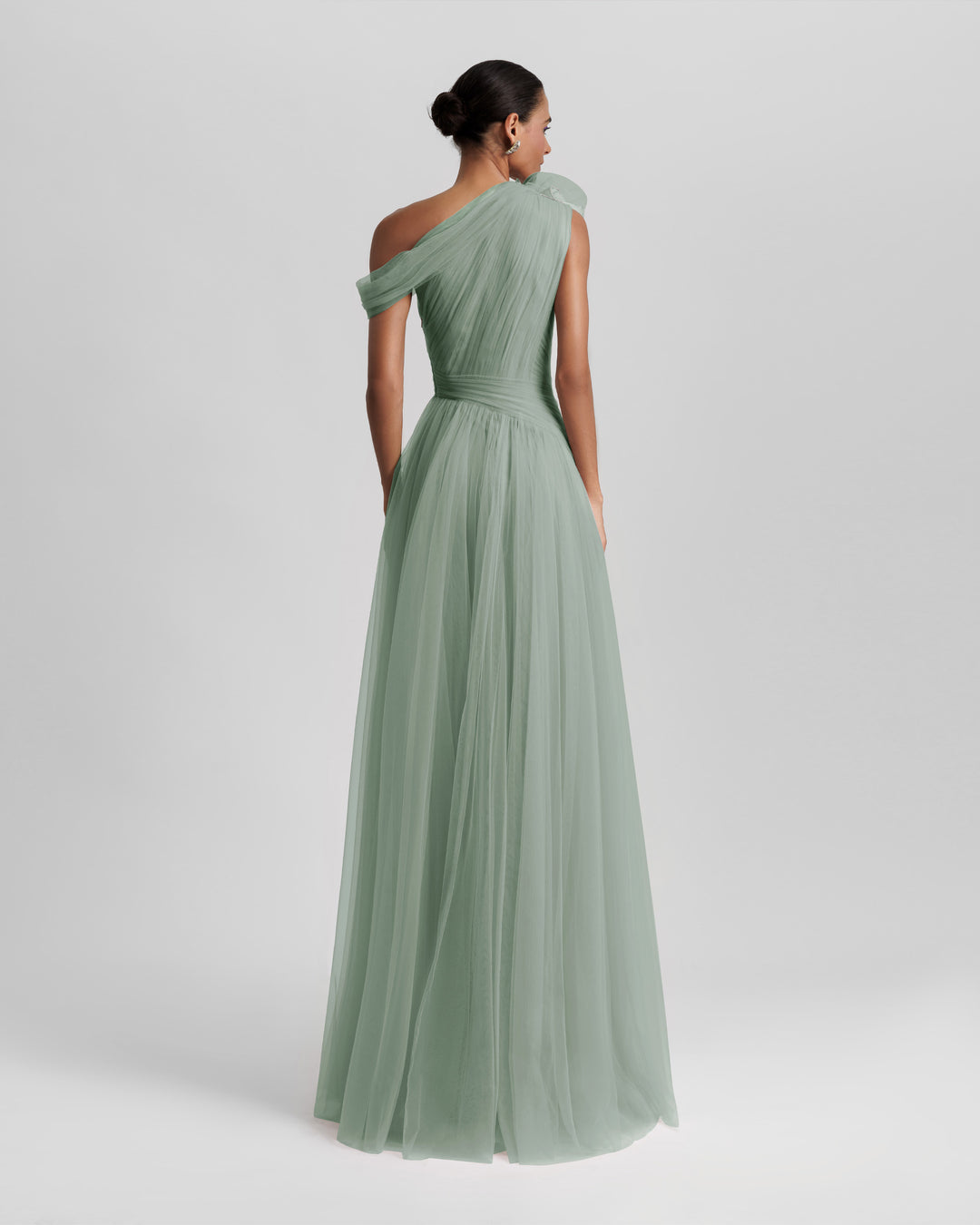 The back of a full tulle long evening dress in mint color, with an asymmetrical neckline and a draping design on the bodice.