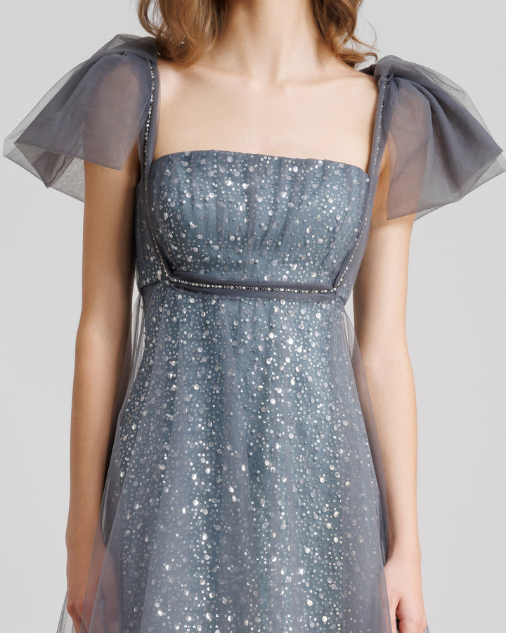 A close-up of a loose-cut grey dress with puffed tulle sleeves and a beaded underlayer.