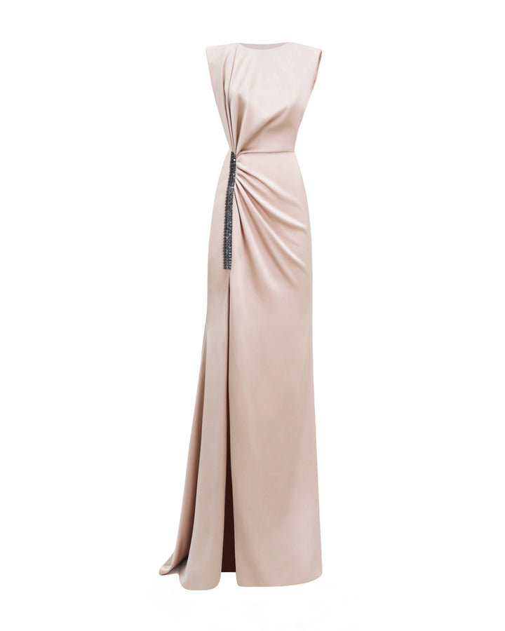 A blush color evening dress with draping on the waist, wide shoulders, and beadings at the side slit.