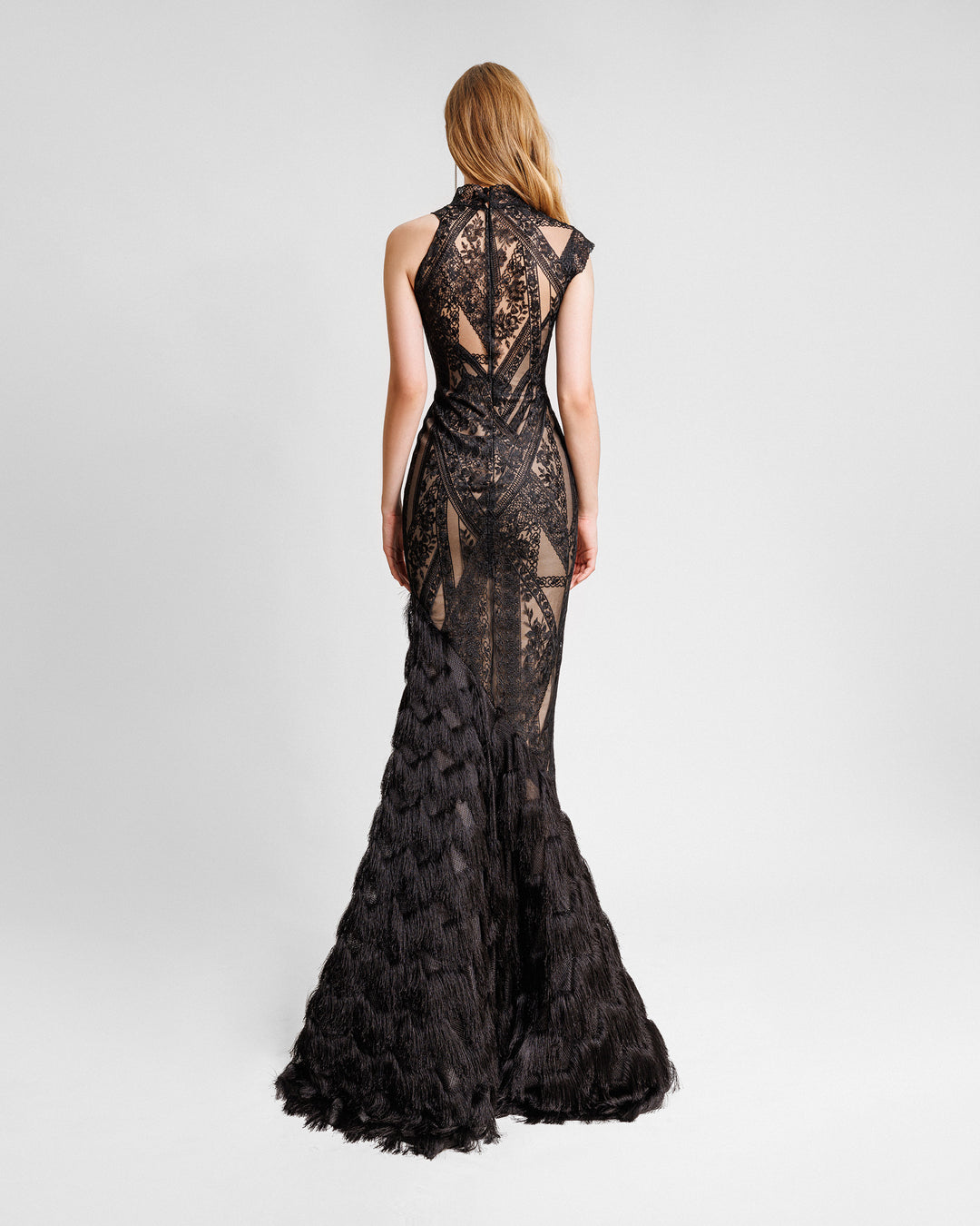 The back of an asymmetrical mermaid cut evening dress in black patterned lace fabric with a single-side fringed hemline.