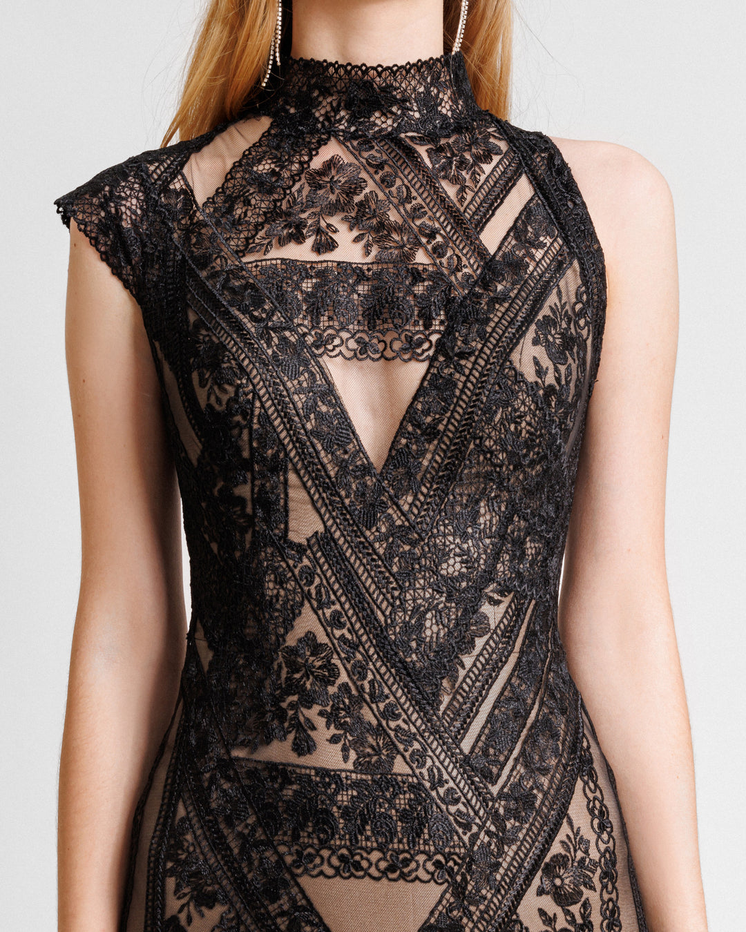 A close-up of an asymmetrical shoulders evening dress in black patterned lace fabric with a high neck.