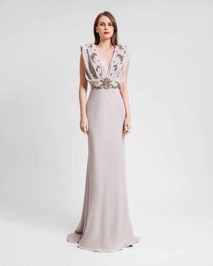 A deep v-neckline griege evening dress with a draped and beaded bodice.