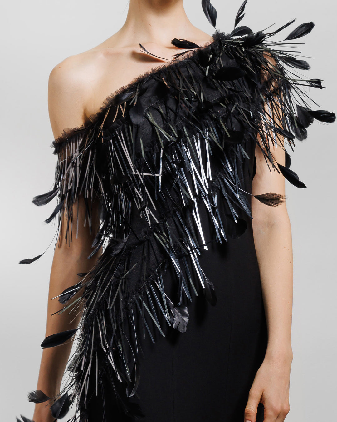 A close-up of an asymmetrical feather neckline black evening dress with flared organza stripes.