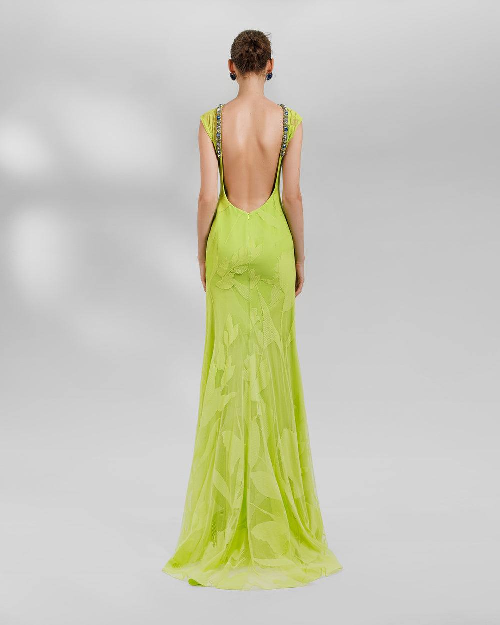 The back of a long patterned lace fabric lime evening dress. It features beads lining the open back.