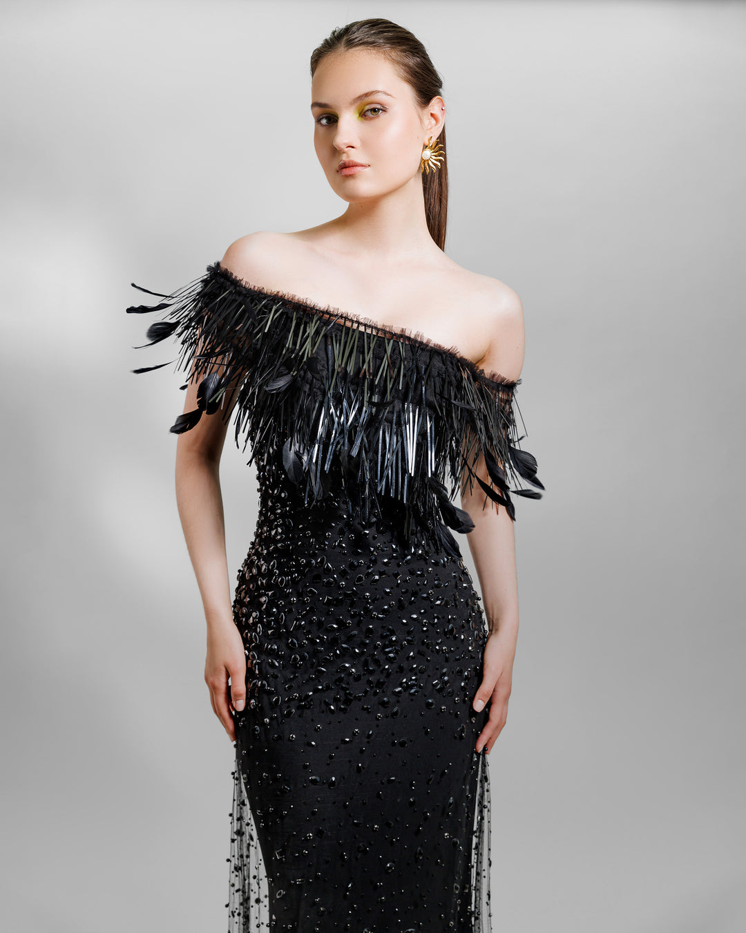 A close-up of an asymmetrical feather neckline fully beaded black evening dress.