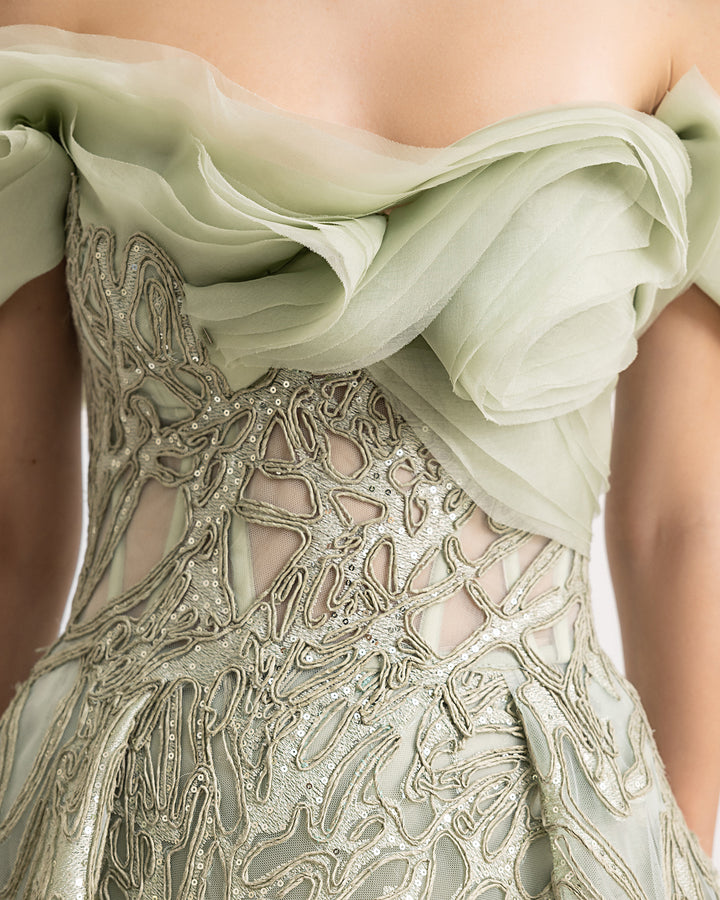 A close-up of an off-the-shoulder sage evening dress with organza draping at the neckline and a draped skirt.