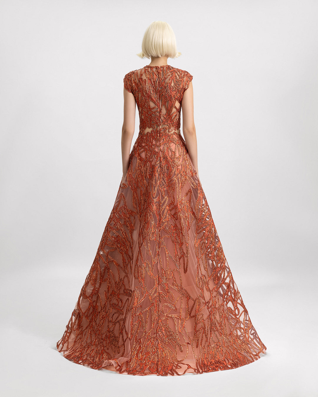 The back of a cap sleeves evening gown in copper color with see-through waist details and a wide skirt.