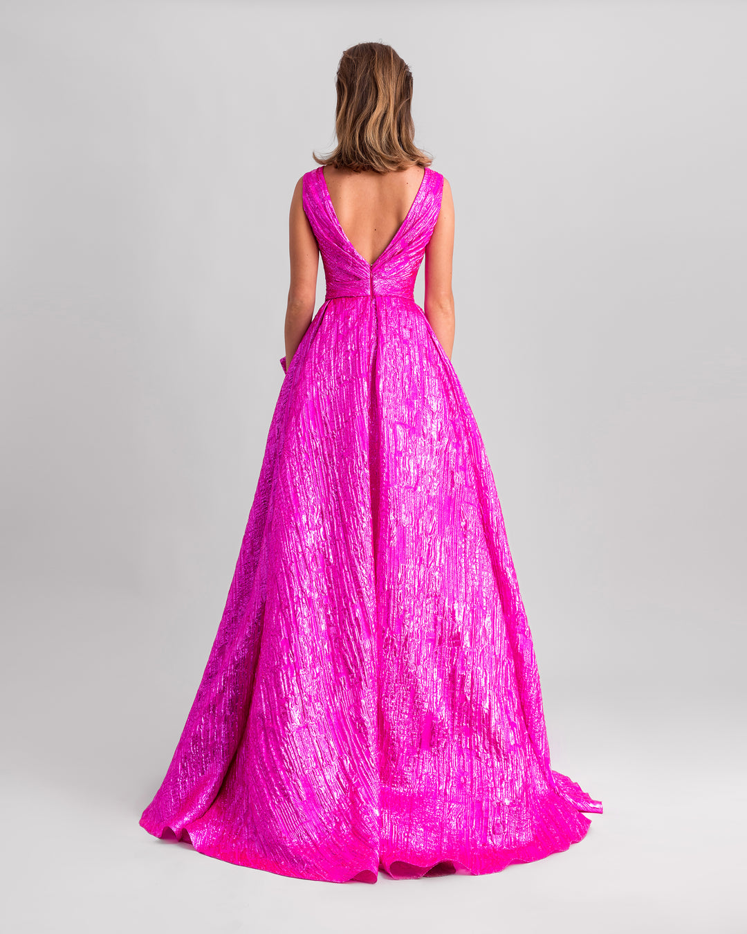 The back of a v-shaped back fuchsia evening dress featuring a wide draped tail.