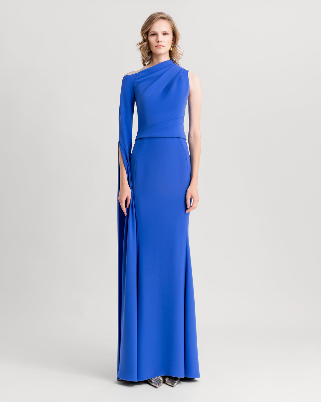 An asymmetrical neckline blue evening dress with draping on the shoulder and waist, and a floor-length sleeve.