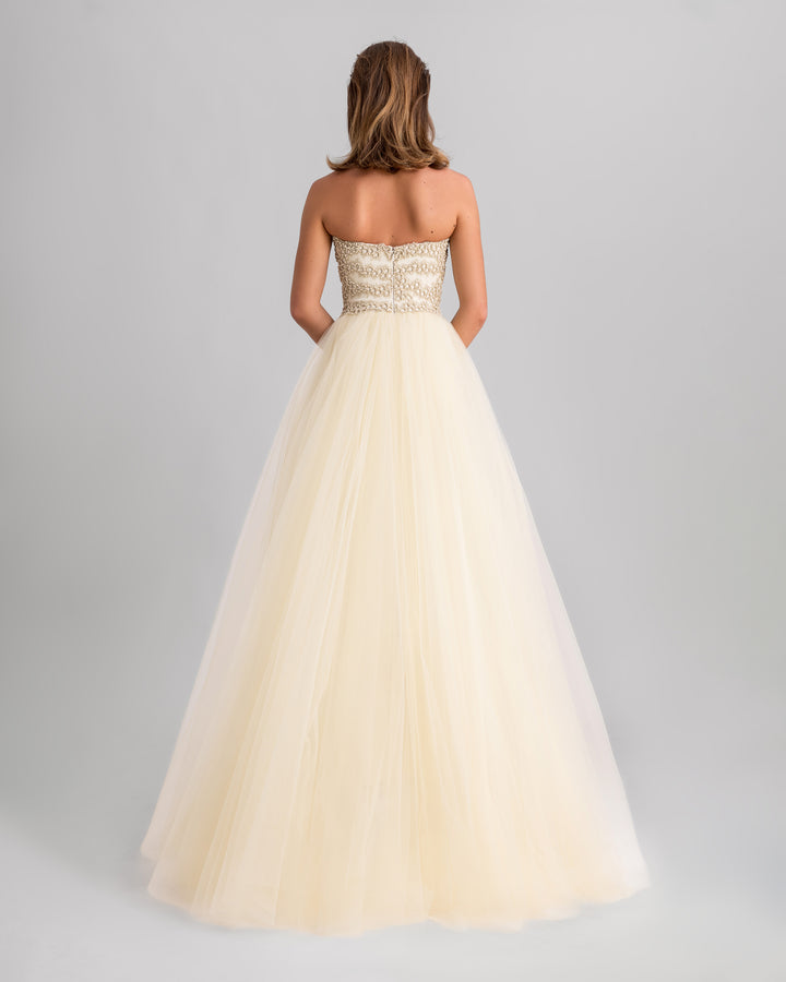 The back of a strapless, fully embroidered slim-cut evening dress in cream, with a flowy tulle tail.