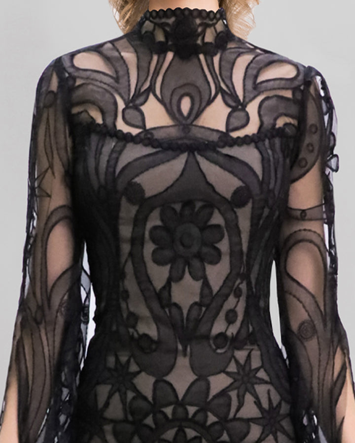 A close-up of a strapless mermaid-cut black patterned lace evening dress with a flared tail, and a detachable top with floor length sleeves.