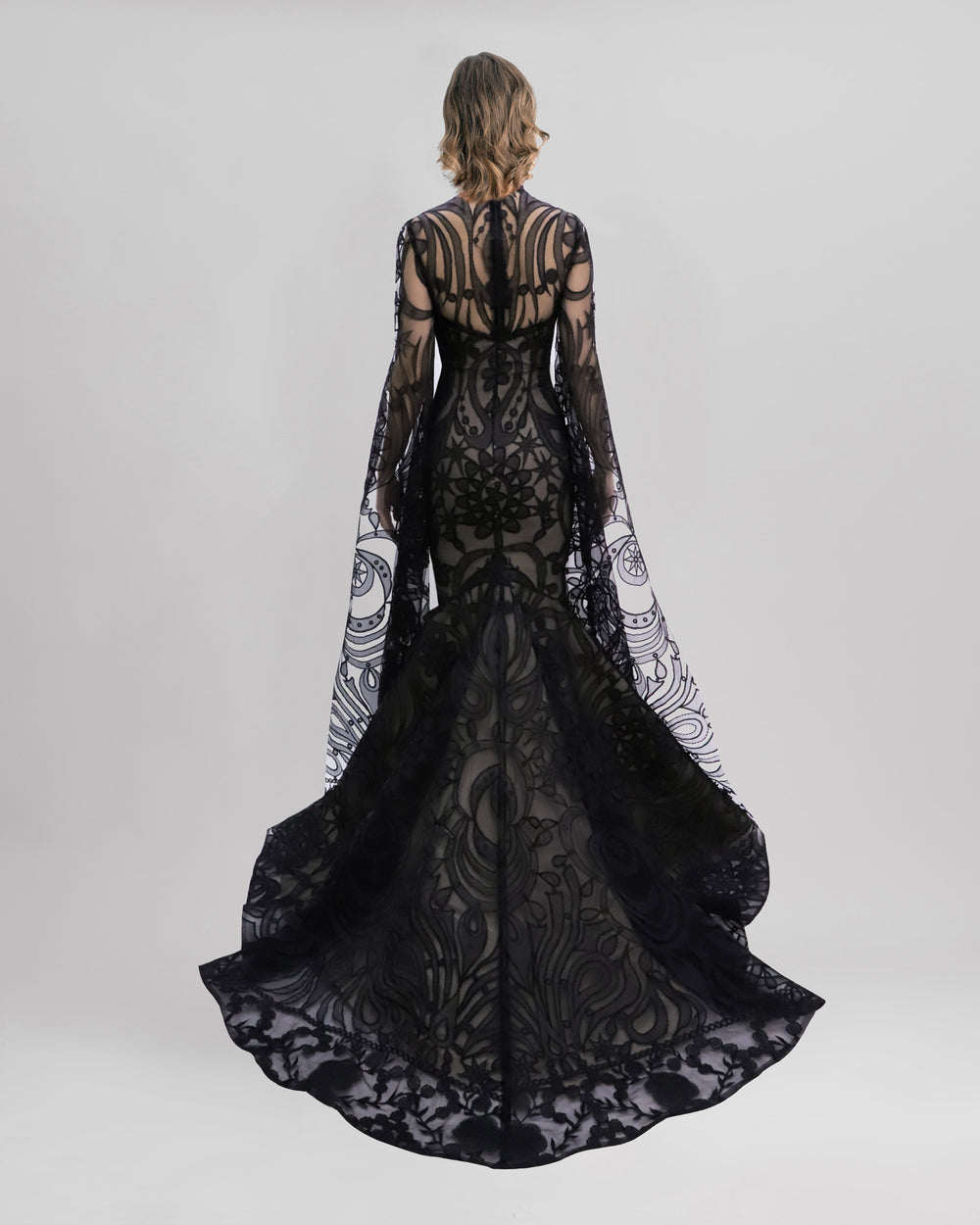 The back of a strapless mermaid-cut black patterned lace evening dress with a flared tail, and a detachable top with floor length sleeves.