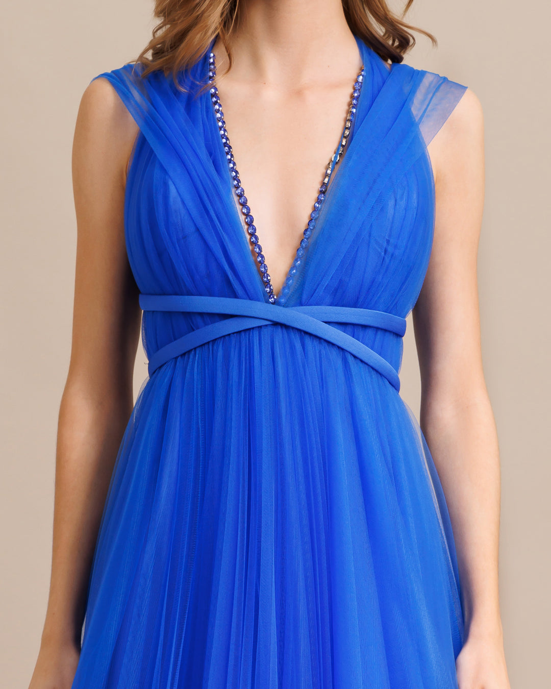 A close-up of a deep v-cut beaded neckline, flared cut tulle long blue dress with ribbon design on the waist.