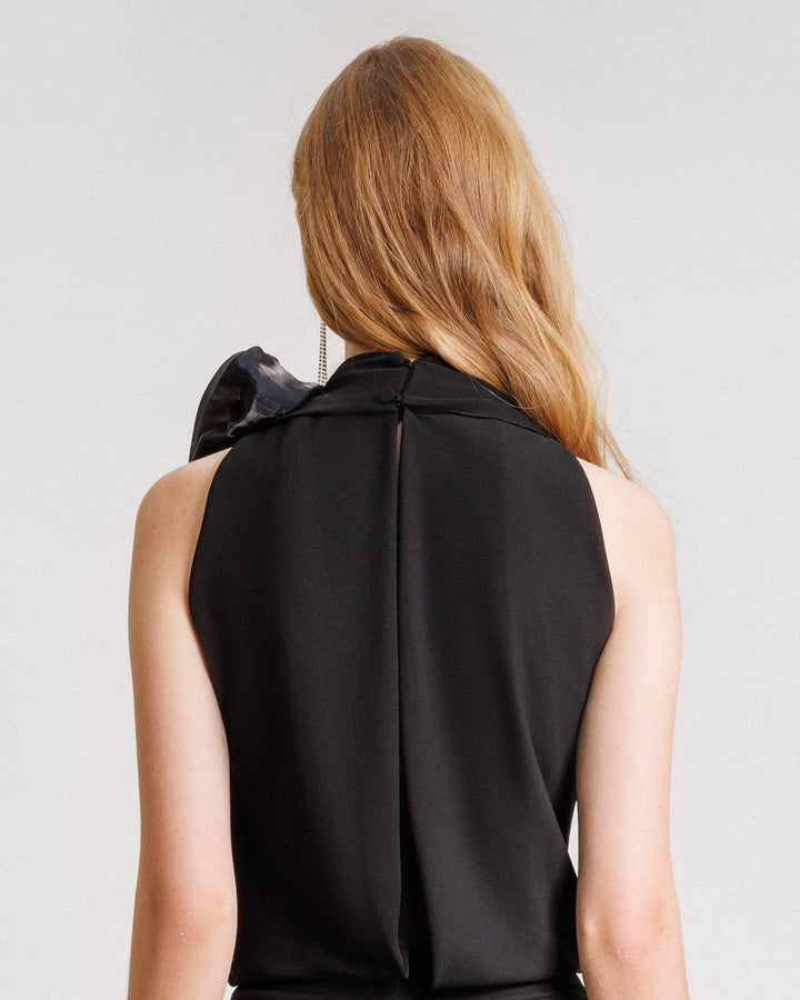 The back of a draped loose black top with draped florals on the shoulder.