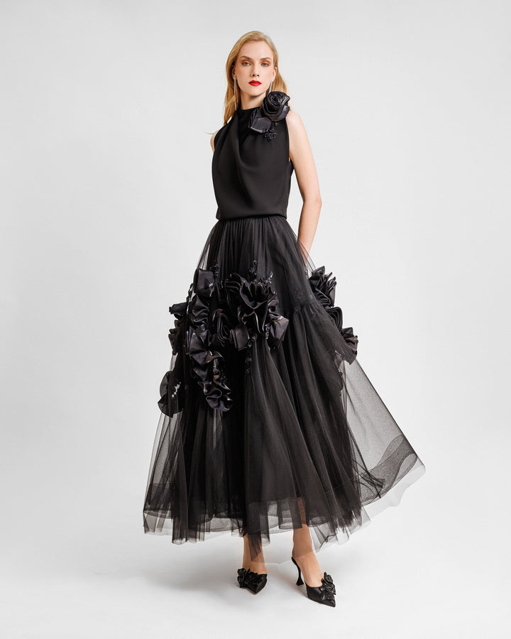 An evening wear set featuring a draped loose top with florals on the shoulder and a black tulle skirt with floral draping.