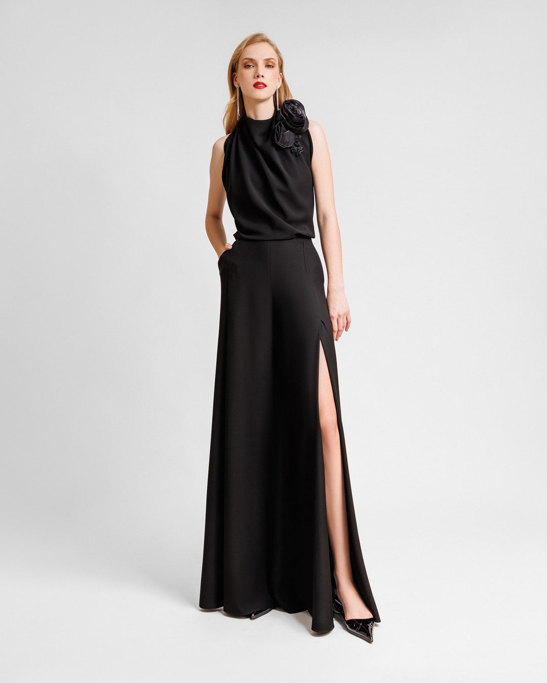 An evening wear set featuring a draped loose black top with draped florals on the shoulder paired with straight-cut pants with slits on the sides.