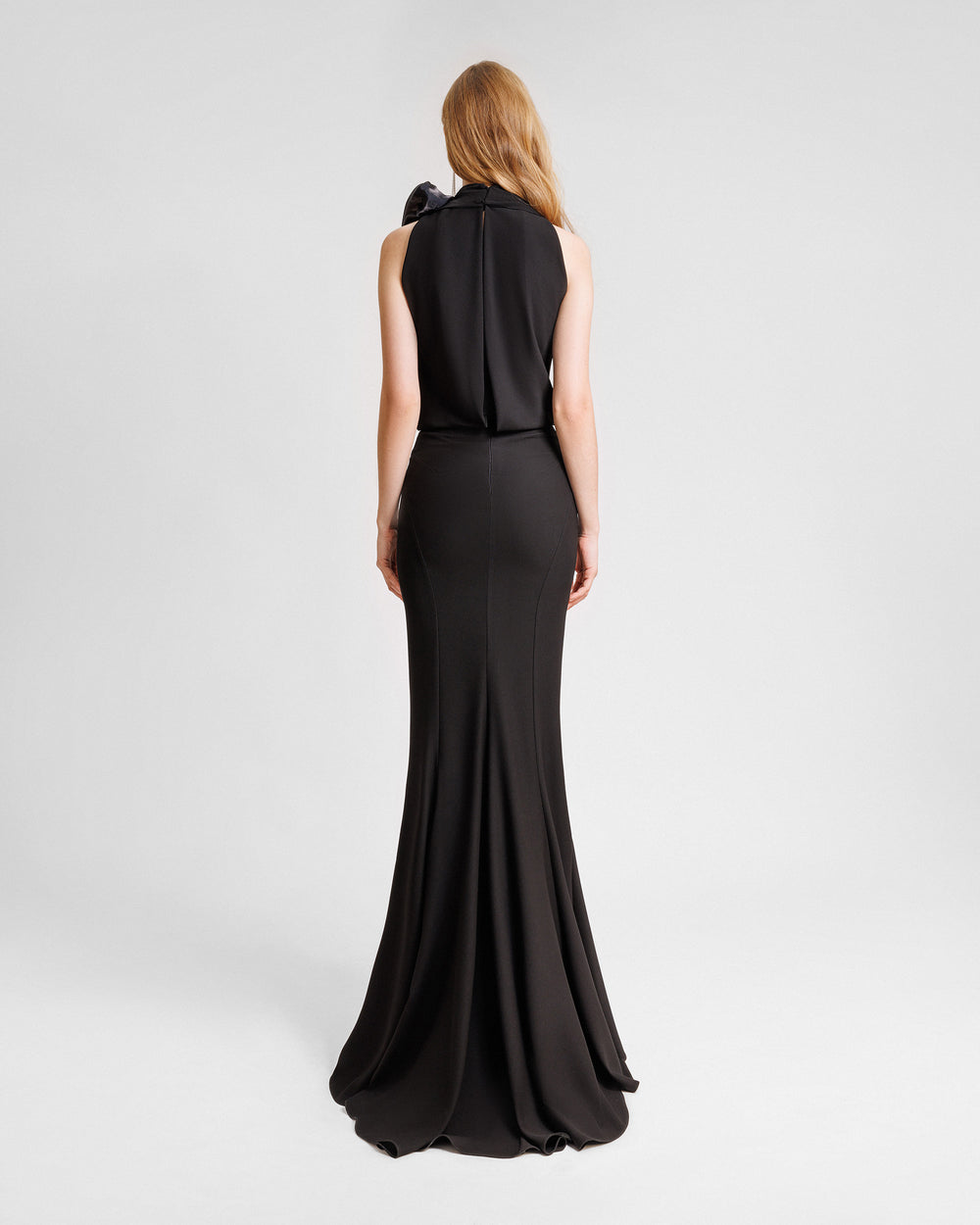 The back of a long crepe black dress with a draped loose bodice featuring draped florals on the neckline and a straight-cut skirt.